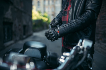 Male biker in leather jacket puts on gloves