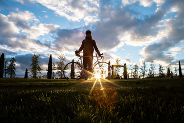 Silhouette of young man standing with bicycle in park on sunset