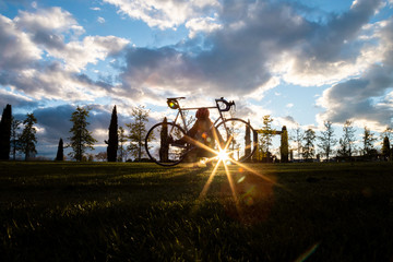 Silhouette of young man standing with bicycle in park on sunset