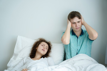 Caucasian Couple on bed with white mattress woman snoring loud makes man feel annoyed. Causes...