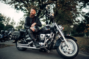 Baerded biker poses on chopper leaning on a helmet