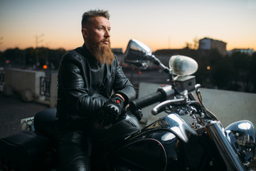 Fototapeta na wymiar Biker poses on a motorcycle in city on sunset