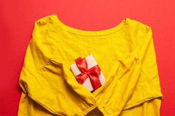 Women's yellow cotton blouse and and gift box on red background. Flat lay, top view, copy space