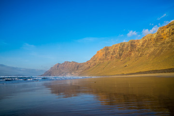Fototapeta na wymiar Spain, Lanzarote, Popular surfing beach famara reflecting impressive famara mountains
