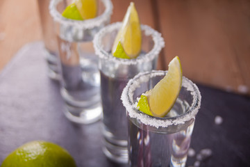 Tequila shot with lime and sea salt on black tray, selective focus
