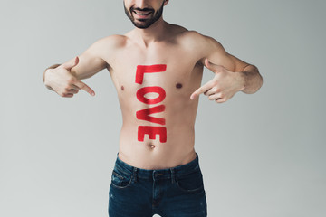 cropped view of smiling shirtless man pointing with fingers at inscription on body isolated on grey