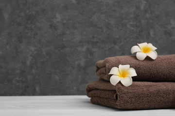 Stack of soft clean towels with beautiful flowers on table against color background. Space for text