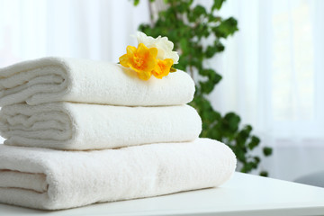 Stack of fresh towels with flowers on table indoors. Space for text