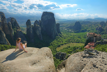 AERIAL: Tourist girl sits on top of a cliff and observes the stunning landscape.