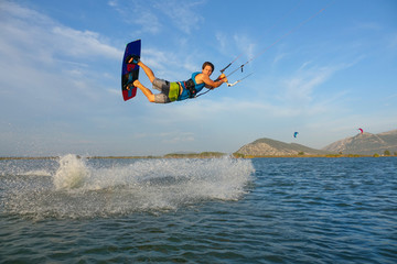 Cool kitesurfer catches a strong wind blowing along shore and jumps high in air.
