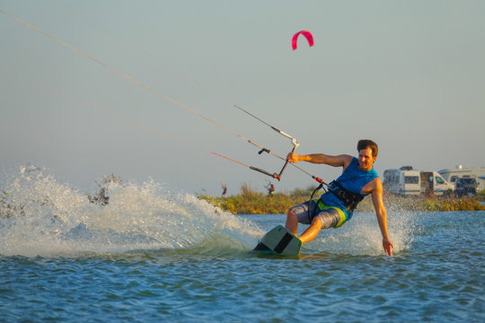 Cool male kitesurfer drags his hand along the calm surface of the blue ocean.