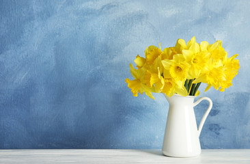 Bouquet of daffodils in jug on table against color background, space for text. Fresh spring flowers