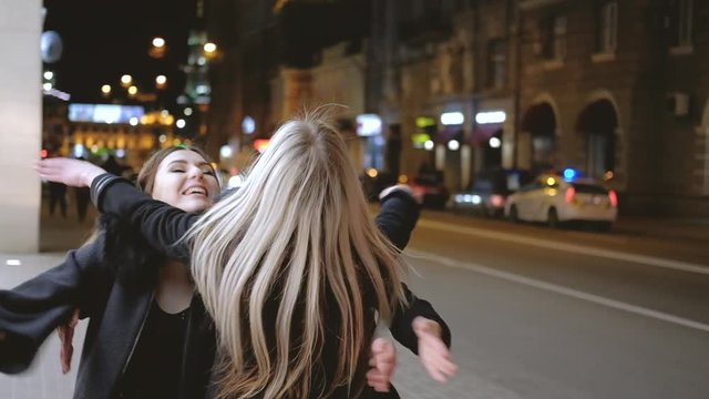Girls night out. Ladies happy to meet their bestie on the street, hugging each other. Blur city lights background.