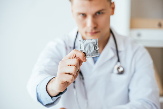 selective focus of serious doctor in white coat holding condom in hand