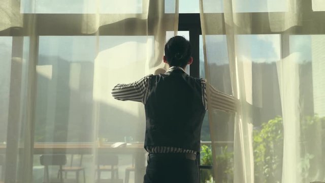asian man opening up curtains walking out to balcony looking at scenery.