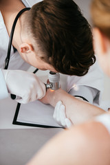 selective focus of dermatologist holding dermatoscope and examining woman with melanoma