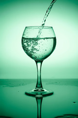 Wine glass with flowing water (white wine) on a background of green gradient