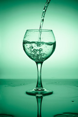 Wine glass with flowing water (white wine) on a background of green gradient