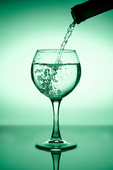 Wine glass with flowing water (white wine) on a background of green gradient