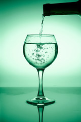 Wine glass with flowing water (white wine) on a background of green gradient