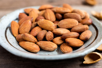 Roasted almonds, salt in dish of green on a wood table. Almonds are rich in nutrients, vitamins and minerals that are essential to the body.