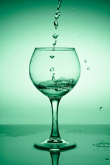 Wine glass with flowing water (white wine) on a background of green gradient