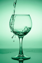 Wine glass with flowing water (white wine) on a background of green gradient