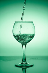 Wine glass with flowing water (white wine) on a background of green gradient
