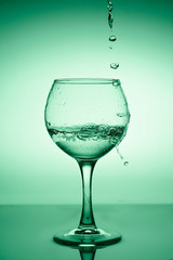Wine glass with flowing water (white wine) on a background of green gradient