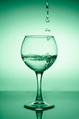 Wine glass with flowing water (white wine) on a background of green gradient