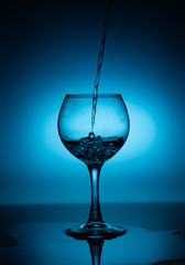 Wine glass with flowing white wine (water) on a blue gradient background