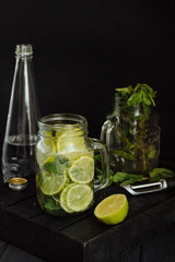 lemonade with lime, slices and circles of sliced lemon in a glass and a mug of lemonade. Mint, lime, soda on a dark background