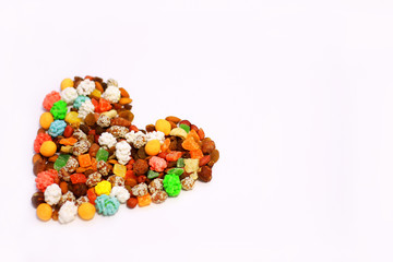 nuts, dried fruits, sweets laid out in the shape of a heart on a white background healthy and unhealthy food concept