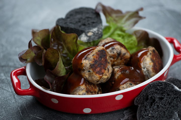 Roasted mushrooms and cheese truffles served with salad leaves in a red bowl, close-up