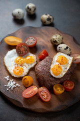 Grilled marbled beefsteak with fried quail eggs and cherry tomatoes, close-up, selective focus