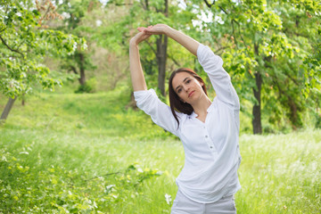 Young woman enjoying nature in a park. Beautiful Girlin white with arms up. Outdoor image.