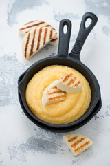 Cast-iron grill pan with polenta and sliced grilled cheese, elevated view over white concrete background