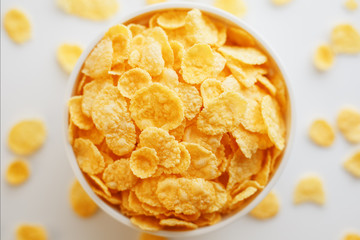 White cup with golden corn flakes, isolated on white background. Hopya crumbled around the cup. View from above