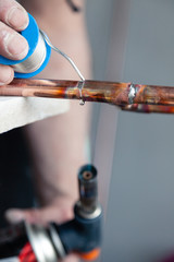 Closeup professional master plumber holding flux paste for soldering and brazing seams of copper pipe gas burner. Concept installation and repair of an apartment building pipeline, leakage