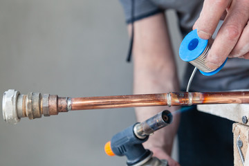 Closeup professional master plumber holding flux paste for soldering and brazing seams of copper pipe gas burner. Concept installation and repair of an apartment building pipeline, leakage