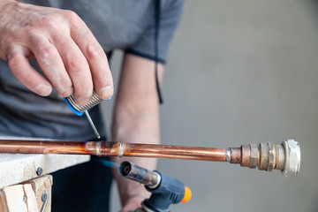 Closeup professional master plumber holding flux paste for soldering and brazing seams of copper pipe gas burner. Concept installation and repair of an apartment building pipeline, leakage