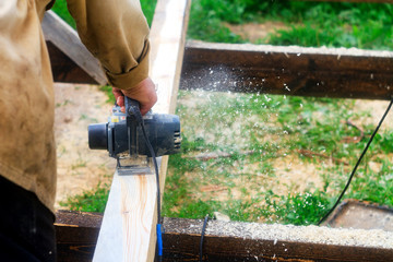 Man working with an electric planer. Processing of wood material, shavings and sawdust scatter in different directions