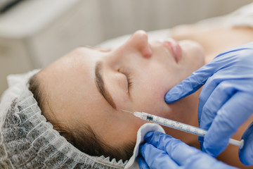 Obraz na płótnie Canvas Closeup portrait injection on face of pretty woman during botox procedures in salon. Professional work, hands in blue gloves, doctor, rejuvenation, modern medicine, making beauty, healthcare