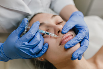 Closeup portrait young woman doing botox procedures by professional. Injection, making lips, modern...