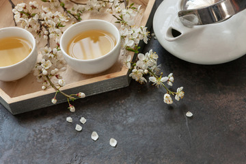 Close up of White porcelain Asian tea set with green Japan tea with cherry blossoming branches on dark background..