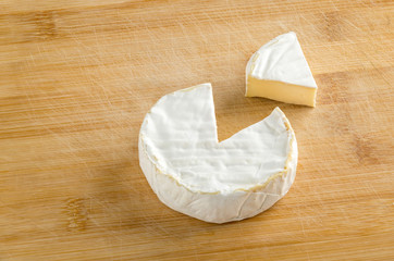 Camembert with piece on wooden chopping board