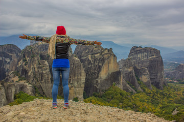 Naklejka premium tourist girl back to camera on cliff edge freedom pose on dramatic picturesque mountains scenery landscape background 
