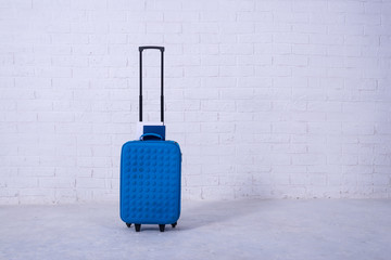 Blue suitcase near the white brick wall.
