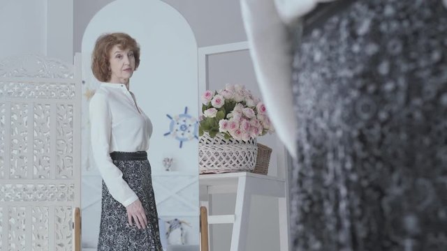 Pretty elegant mature woman looking in the mirror, examining her reflection. The lady looking at her new long skirt in the mirror. Lovely woman spinning at the mirror