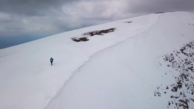 Aerial drone shot of a man walking on the edge of snow mountain.